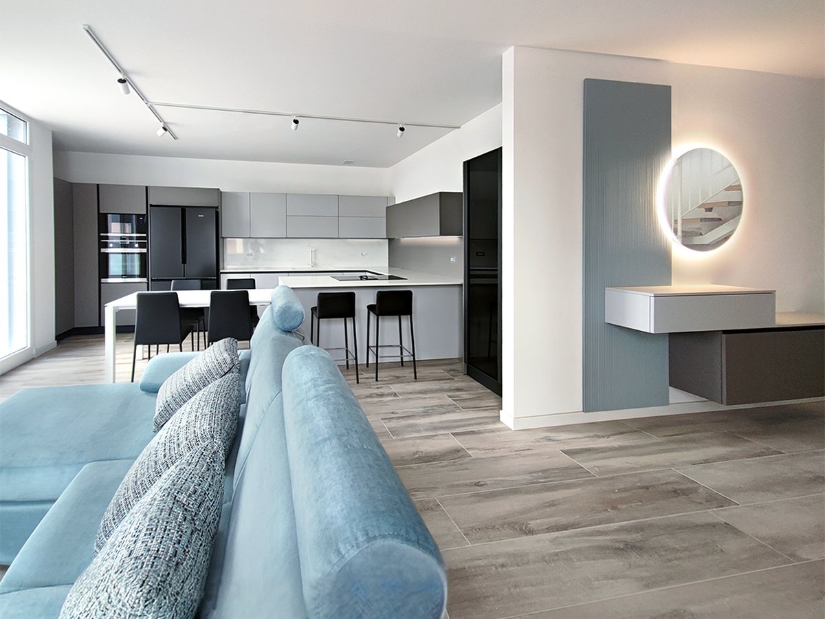 Zona giorno con divano azzurro aperta sulla cucina, con consolle sospesa e specchio tondo retroilluminato